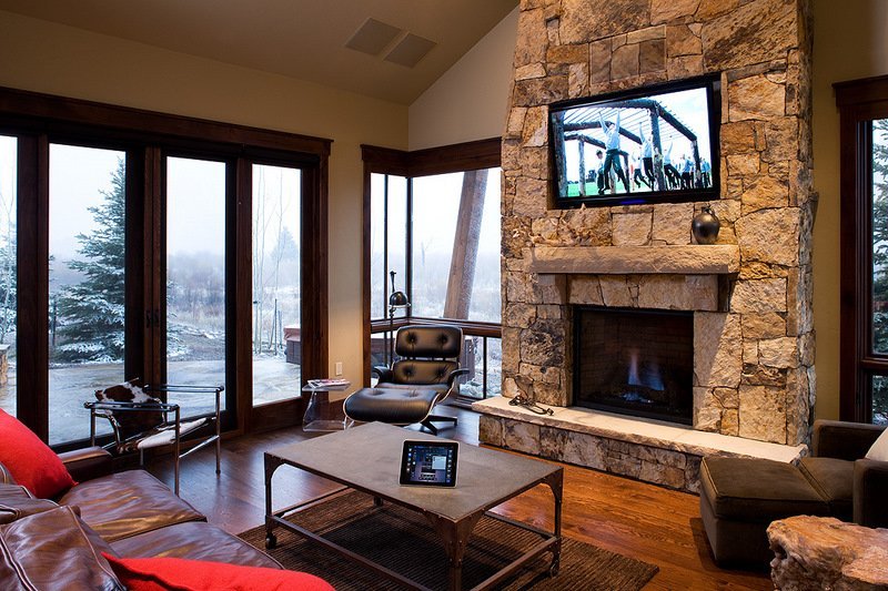 Television above a stone fireplace beside mountain-facing windows